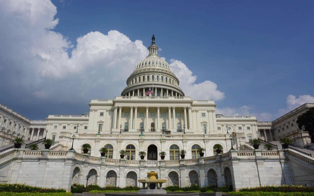 The image shows the United States Capitol building in Washington, D.C., featuring its iconic white dome topped with a statue. The building has grand columns and multiple windows, with a well-maintained garden and fountain in the foreground under a partly cloudy sky—an emblem of democracy amidst debates on 2022 Income Limits.